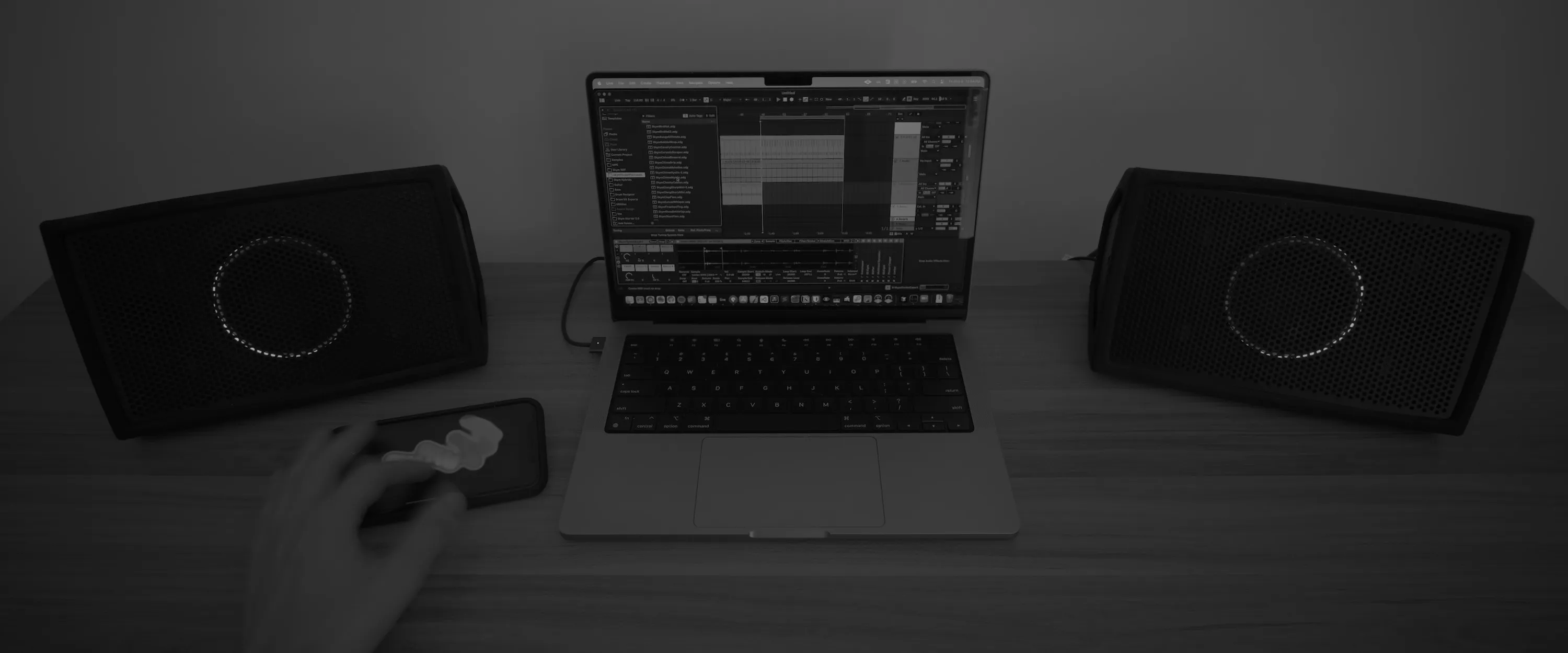 A hand playing Skym on an iPhone next to a MacBook running Ableton Live, between two studio monitors